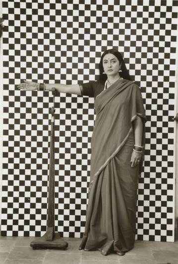 A person in a sari standing in front of a checkered wall

Description automatically generated